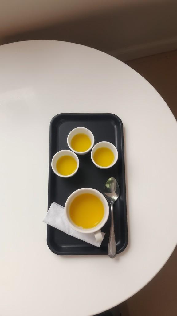 Three cups with a bright yellow liquid on a black tray, atop a white table.