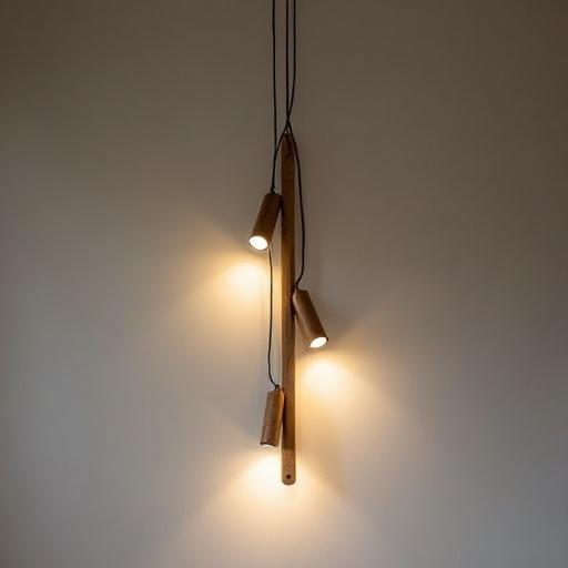 Professional vertical suspension light suitable for church use. Centered vertical track rail holds three adjustable tubular spotlights. Each spotlight has a brass/golden finish. Track is adorned with hollow brass tubes stacked vertically. Tubes are drilled to allow light passage. Rotating rings permit orientation of tubes and spotlights. Suspension supported by thin steel cables. Horizontal rods fix brass tubes creating a long, simple tube appearance, revealing spotlights and evoking a Latin cross.