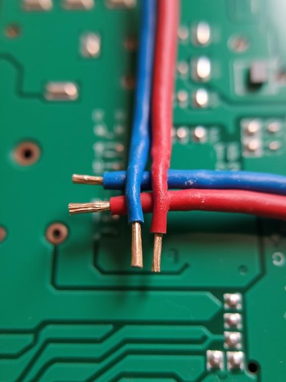 A pair of blue and red wires twisted together on a green PCB