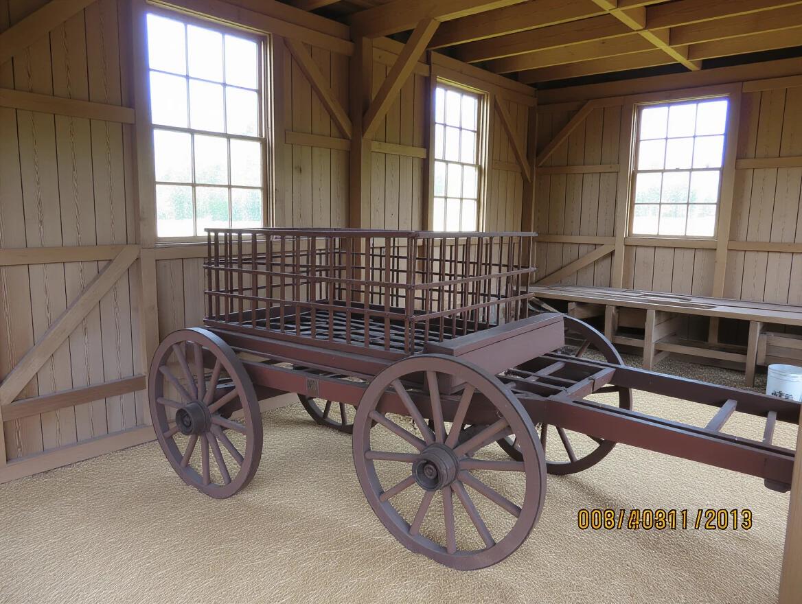 View from inside the barn built in 1890. Wooden wagon placed centrally features a metal cage made of bars. Barn interior has wooden walls and windows.