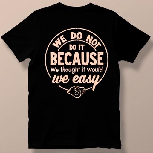 Black t-shirt with a circular design on the back. Features bold light peach lettering. Contains the phrase We do not do it because it's easy. Below is the phrase We do it because we thought it would be easy in a script style font. Display emphasizes the humorous motivator.