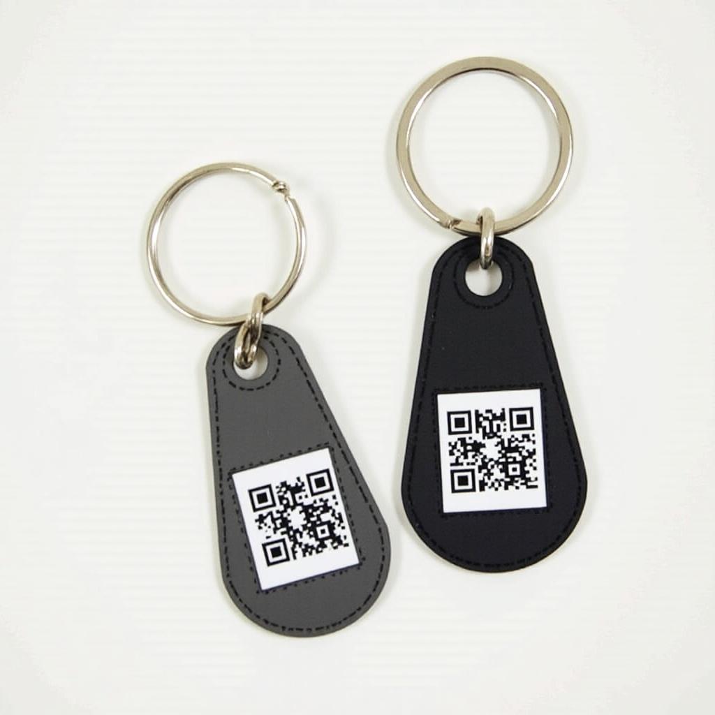 Keychains with QR codes displayed side by side. One is gray, and the other is black.