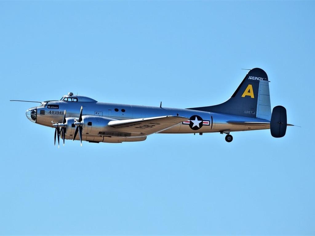 This image features a classic World War II bomber, specifically a B-17 Flying Fortress. The airplane is shown in mid-flight against a clear blue sky. The aircraft has a shiny metal exterior and distinctive military insignia, including star symbols and a unique tail design. The B-17 is known for its large wingspan and multiple engines, giving it a powerful presence in the air. This particular plane has the serial number 483514 and is marked with a blue and black color scheme. It's a historical representation of aviation during a significant time period.