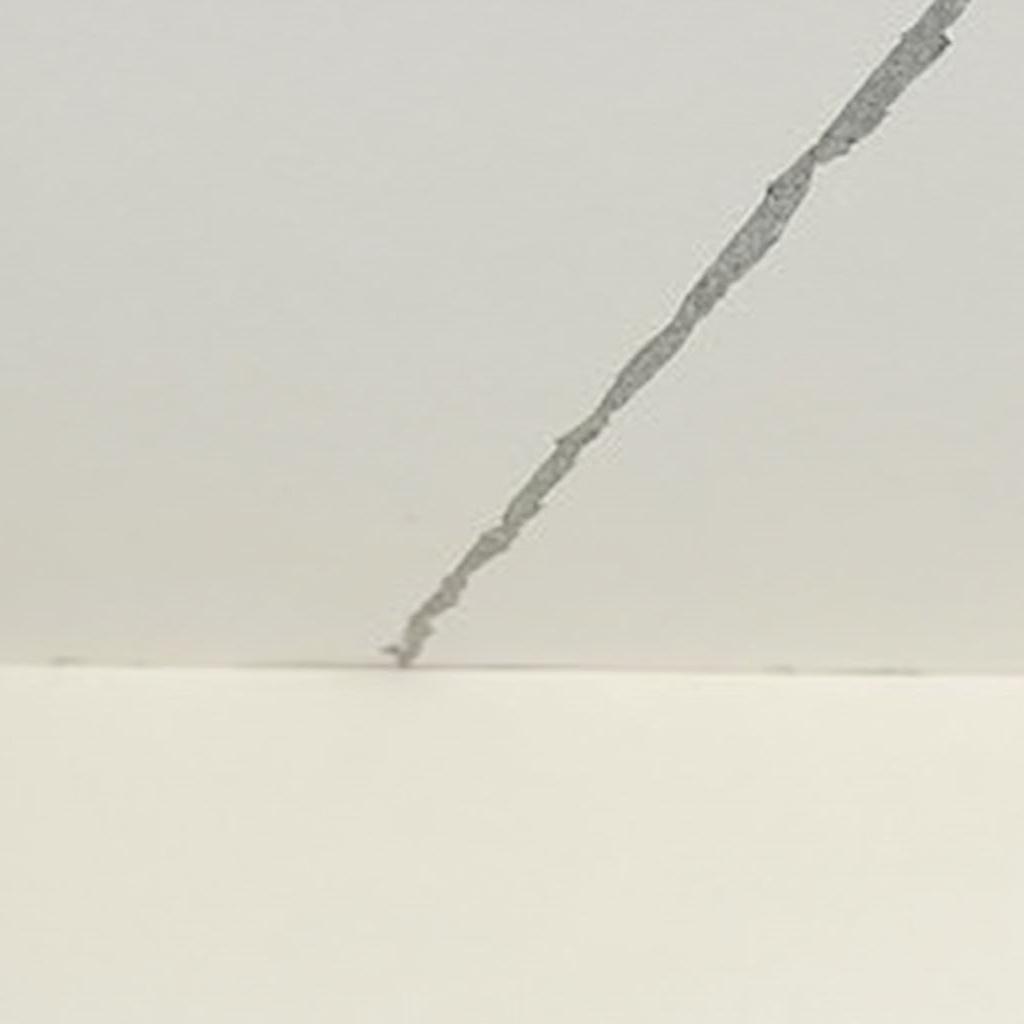 A joint in the ceiling where drywall sheets meet. There is a hairline crack at the seam. Movement in the building can cause these cracks.