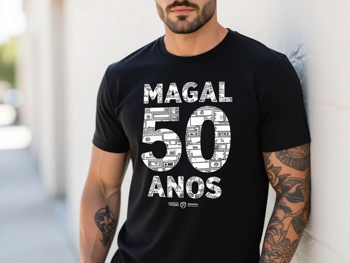 Model has green eyes and dark brown hair and beard. He wears a black t-shirt with white print. The print has modern urban designs. His physique is strong, exuding silent authority. Muscular arms have cassette tape tattoos. He sports a striking red cap with a white '10.' DJ headphones are worn, connecting him with music.
