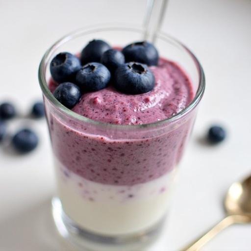 Layered blueberry chia pudding in a glass. Topped with fresh blueberries. Smooth texture with vibrant colors.