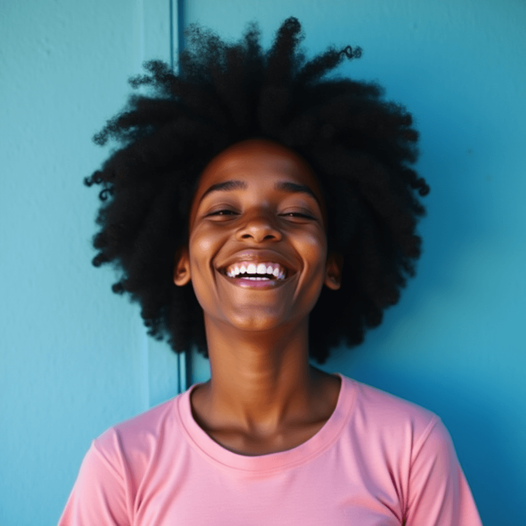 A person with a big smile and vibrant hair stands against a blue background, exuding happiness.