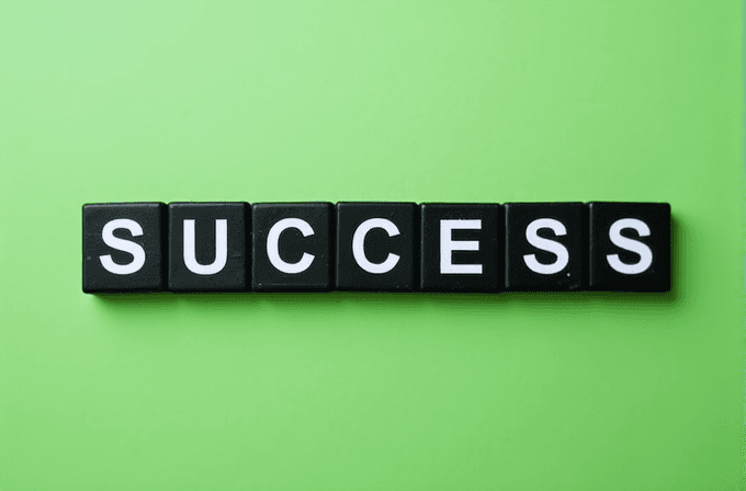 The word 'SUCCESS' is spelled out using black square blocks with white letters against a vibrant green background.