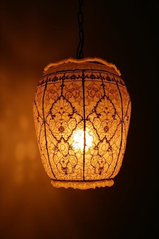 Hanging lamp with intricate lace design illuminated by warm light.