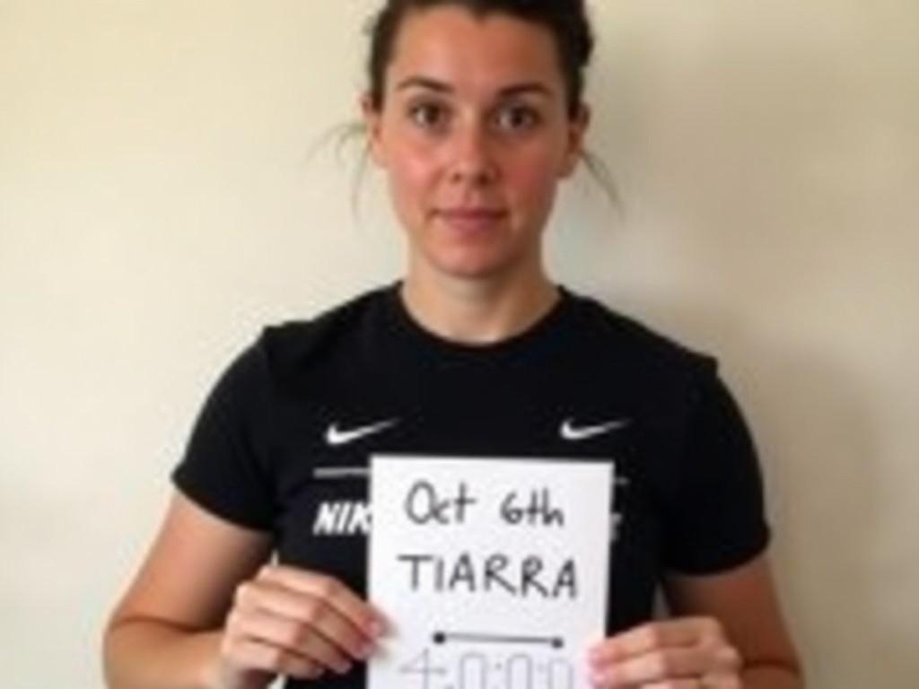 A person holding a sign with the name 'Tiarra' and the date 'Oct 6th', wearing a Nike shirt, with a plain background.