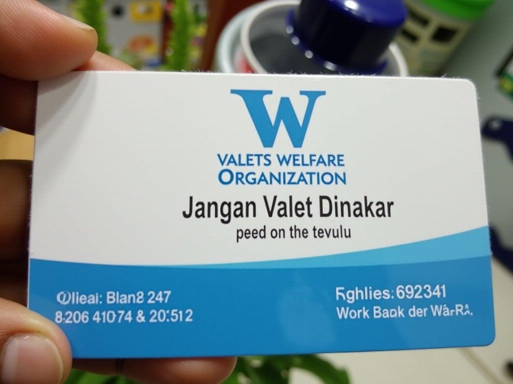 This is a photo of an identification card from 'Valets Welfare Organization'. The card features a blue and white design with the organization’s logo at the top. It includes the name 'Jangan Valet Dinakar' along with the title 'Founder Chairman'. A contact number is visible below the name. The card also has an authorized signature, indicating it is official. The background shows a bit of greenery, and there are items behind the card that are out of focus.