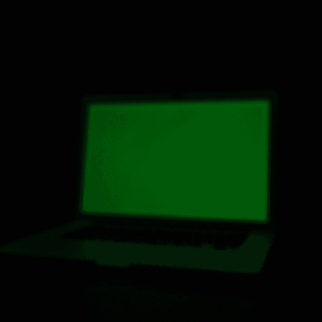 A laptop screen illuminated with a solid green color in a dark environment.