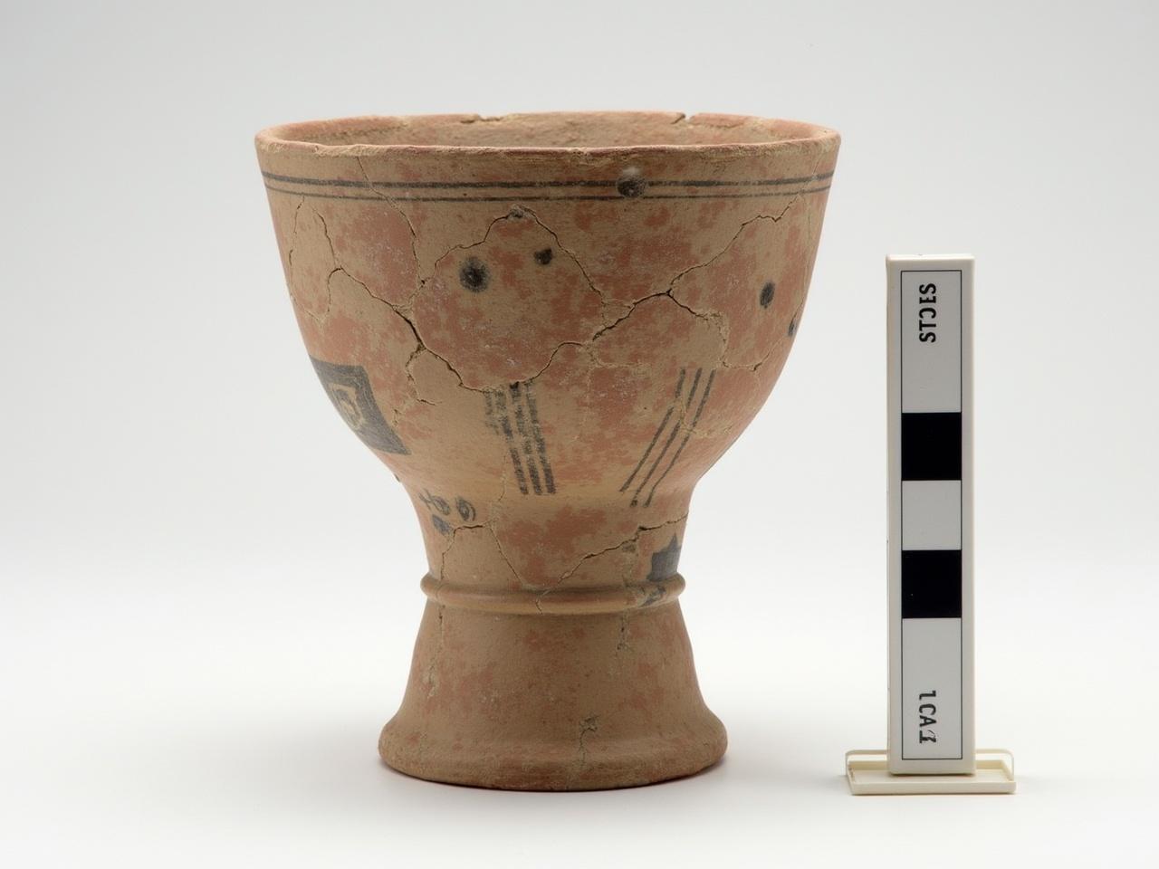 The image shows an ancient ceramic vessel that has been partially reconstructed. The vessel features a wide mouth and a narrow neck, typical of pottery from historical periods. The surface of the pottery is cracked, which indicates that it may be quite old. There are decorative markings and patterns present on the vessel, suggesting that it may have been used for storage or ceremonial purposes. Alongside the vessel, there are measurement indicators to provide scale, showing the size of the object. The background is plain to keep the focus on the vessel.