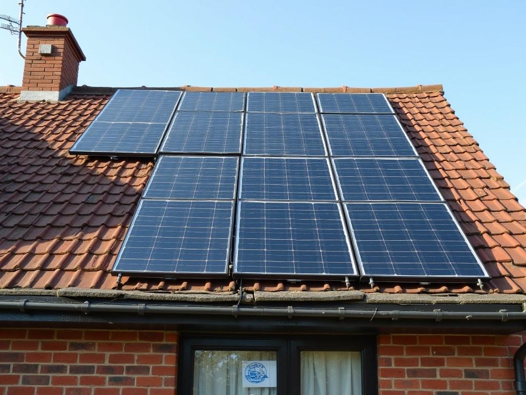 Solar panels installed on a residential roof. Panels are arranged but not positioned well. Visible roof material and chimney. Clear blue sky in the background.