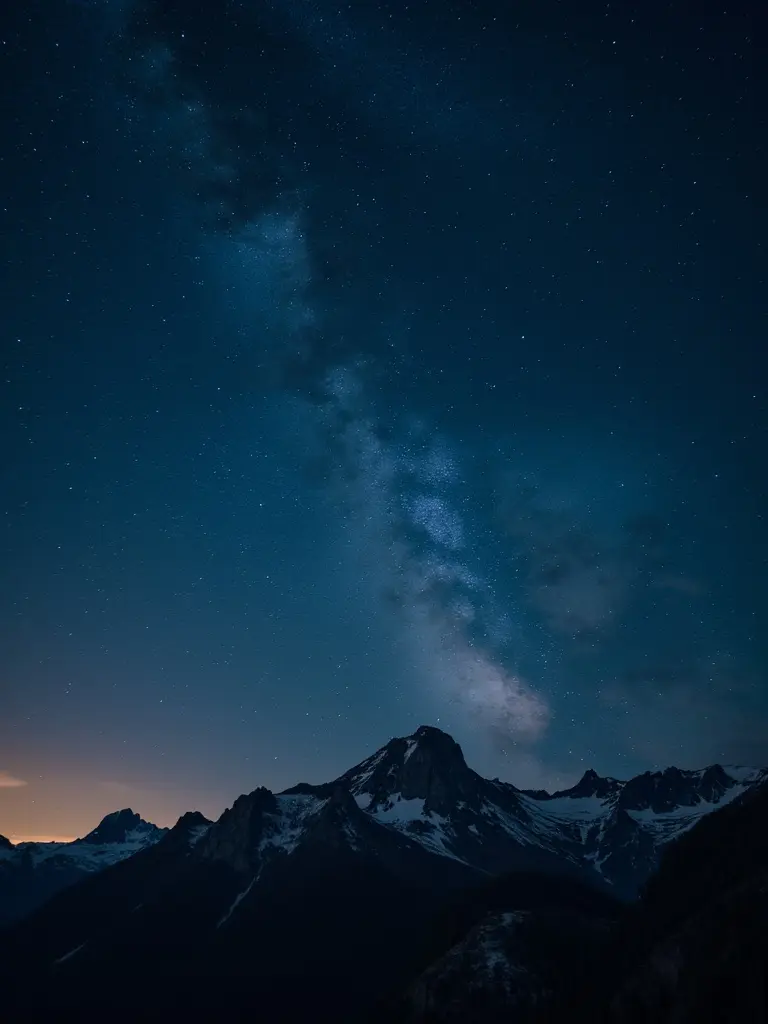 Night sky filled with stars. Milky Way visible above mountain peaks. Snow-capped mountains under a dark sky. A serene and tranquil atmosphere.