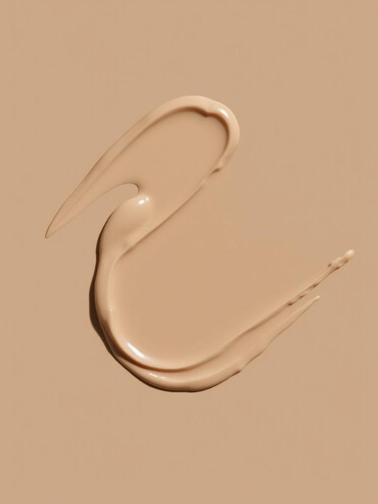 Smooth smear of stick foundation on a beige background. Neutral skin tone swatch displays creamy texture and blendability.