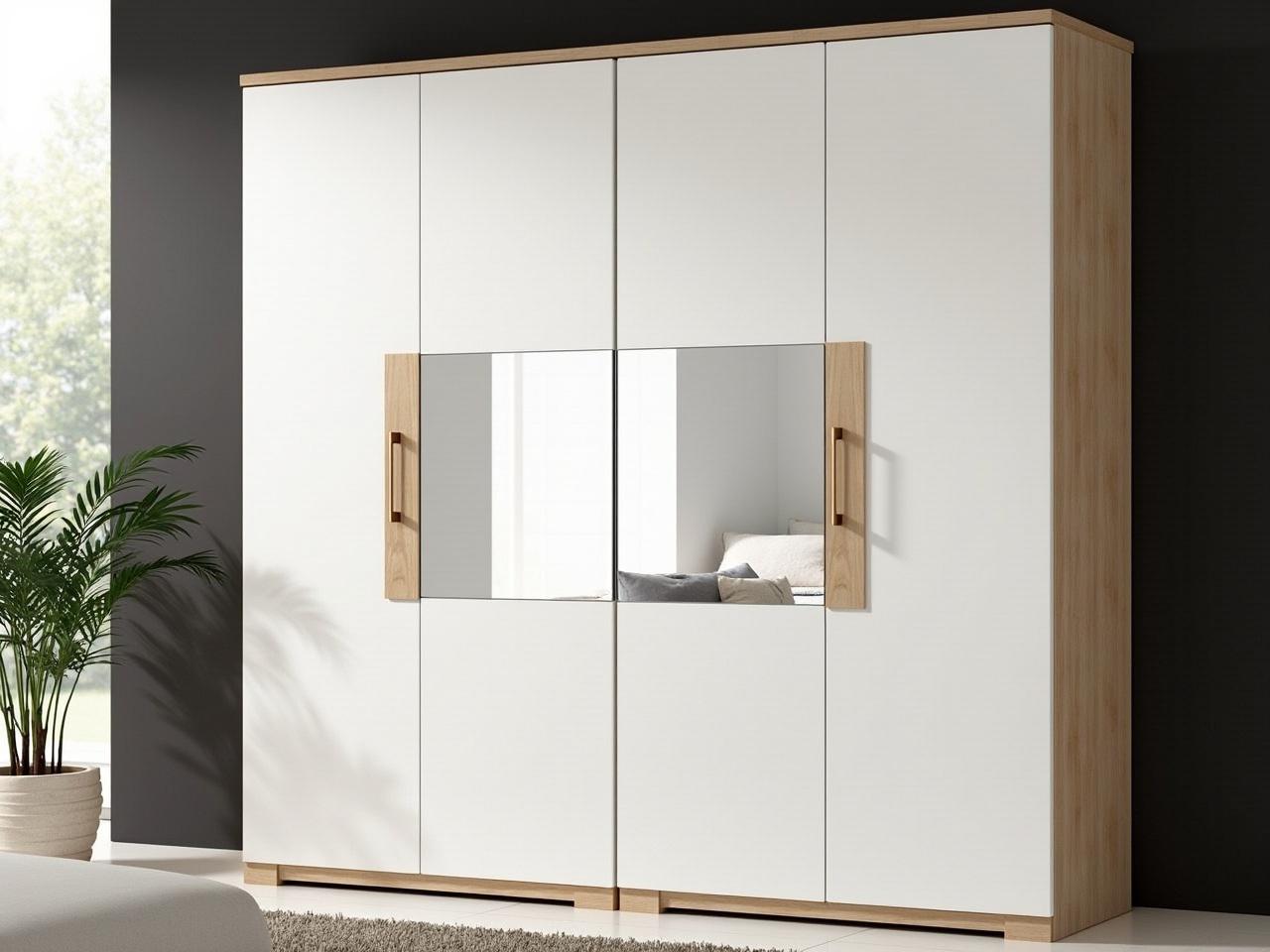 This image shows a modern wardrobe with a combination of white and wooden finishes. The wardrobe has four doors, two of which are white and two are mirrored. The sleek design is complemented by simple wooden handles that add a touch of warmth. The wardrobe stands against a wall that features a dark color, which enhances its contemporary appearance. In front of the wardrobe, a cozy room is suggested with soft lighting and a glimpse of a sofa in the background. A potted plant to the side adds a natural element to the scene.