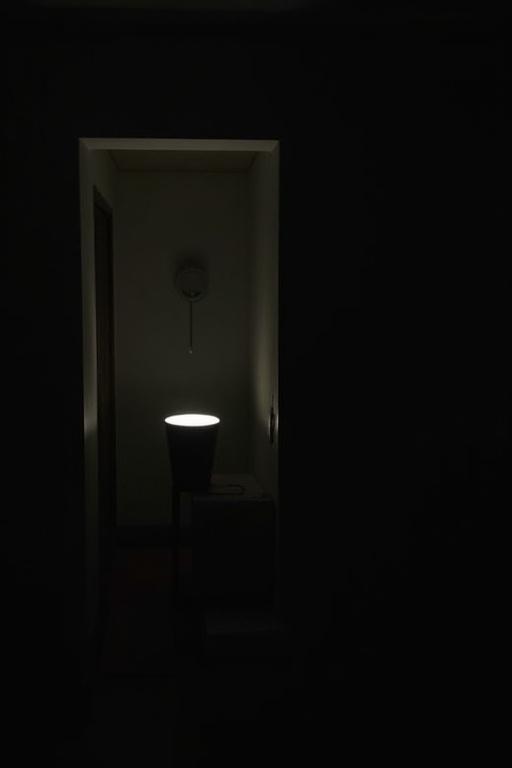 Room in darkness illuminated by soft lamp. Soft silhouette visible in background.