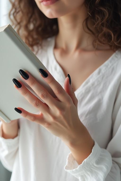 Pale woman with curly hair wears white clothing and reads a book while holding it at face height. One arm lifts the book while her other hand rests on her chest showcasing long almond-shaped black nails. A close-up emphasizes her elegant nails as the main focus of the image.