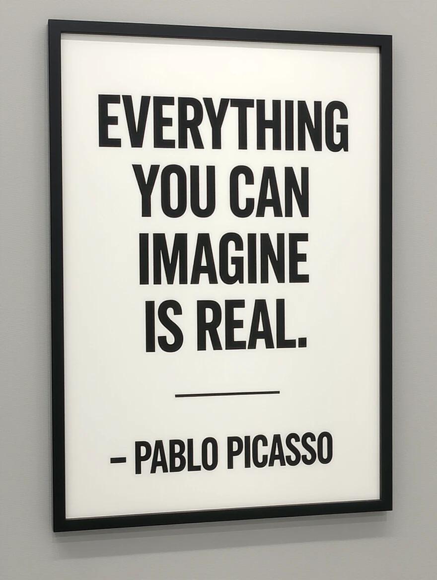 A poster framed in black on a gray wall features a motivational quote. The text reads Everything you can imagine is real. by Pablo Picasso. The poster is minimalist and modern in design.