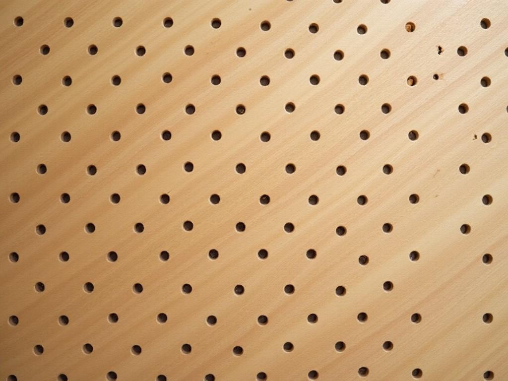 This image features a wooden pegboard background, showcasing a pattern of evenly spaced holes across a smooth surface. The wood showcases a light brown hue with beige tones that add warmth to the image. It’s a perfect representation of a DIY workspace or organizational tool that can enhance various interior design themes. The evenly distributed holes suggest functionality and can inspire creativity for crafting or storing items. Ideal for articles, videos, or projects focused on home organization and decoration.