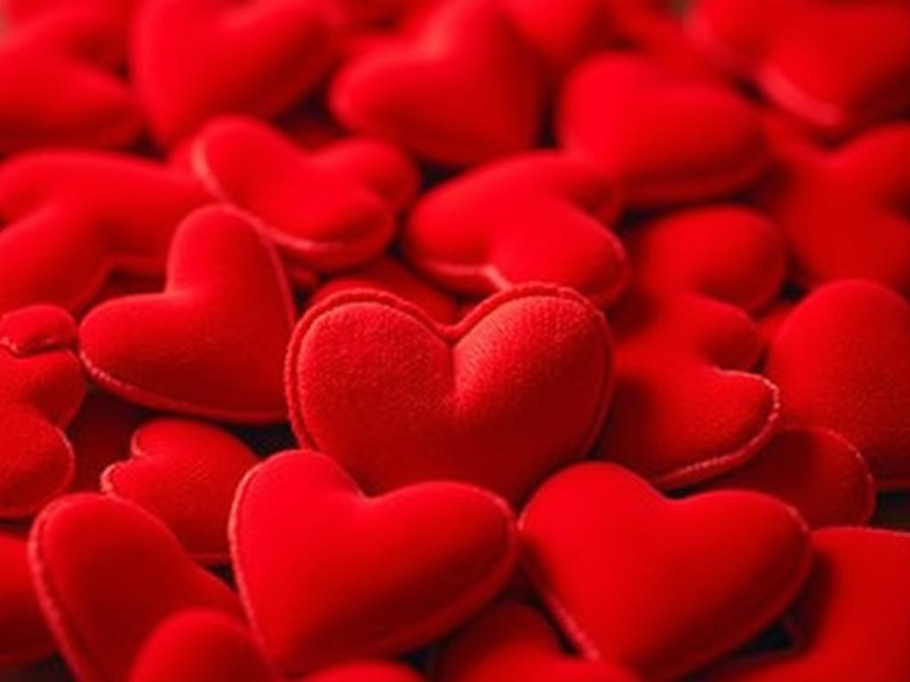 The image shows a vibrant collection of small red fabric hearts piled together. Each heart is plush and soft, resembling a small pillow. They are made from a smooth satin material that catches light beautifully, highlighting their rich red color. Some hearts overlap while others are easily visible, creating a visually appealing texture. The overall feeling of the image is warm and romantic, perfect for conveying love and affection. This imagery could be used for Valentine's Day or other romantic celebrations.