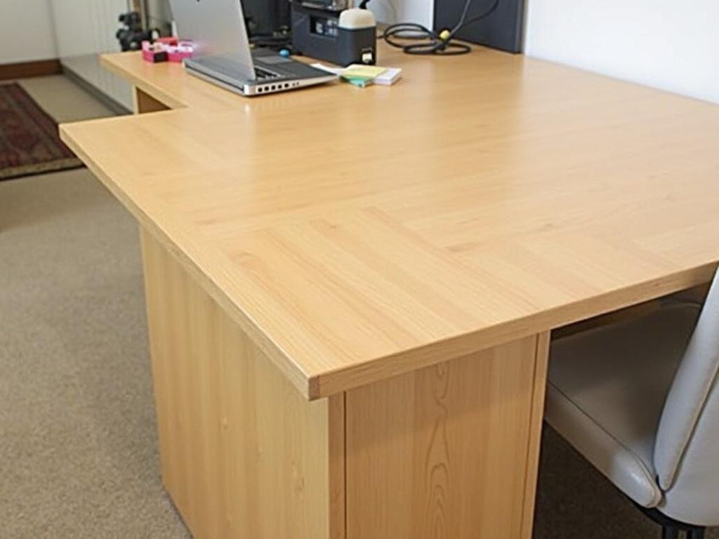 This image shows a wooden counter or desk with a clean finish. The surface appears to have some organizational items placed on it, including a laptop and some stationery. The background features light-colored walls and a rug on the floor. There are also some items stored nearby, hinting at a workspace setup. A chair is partially visible on the right side of the image, suggesting a place to sit and work.