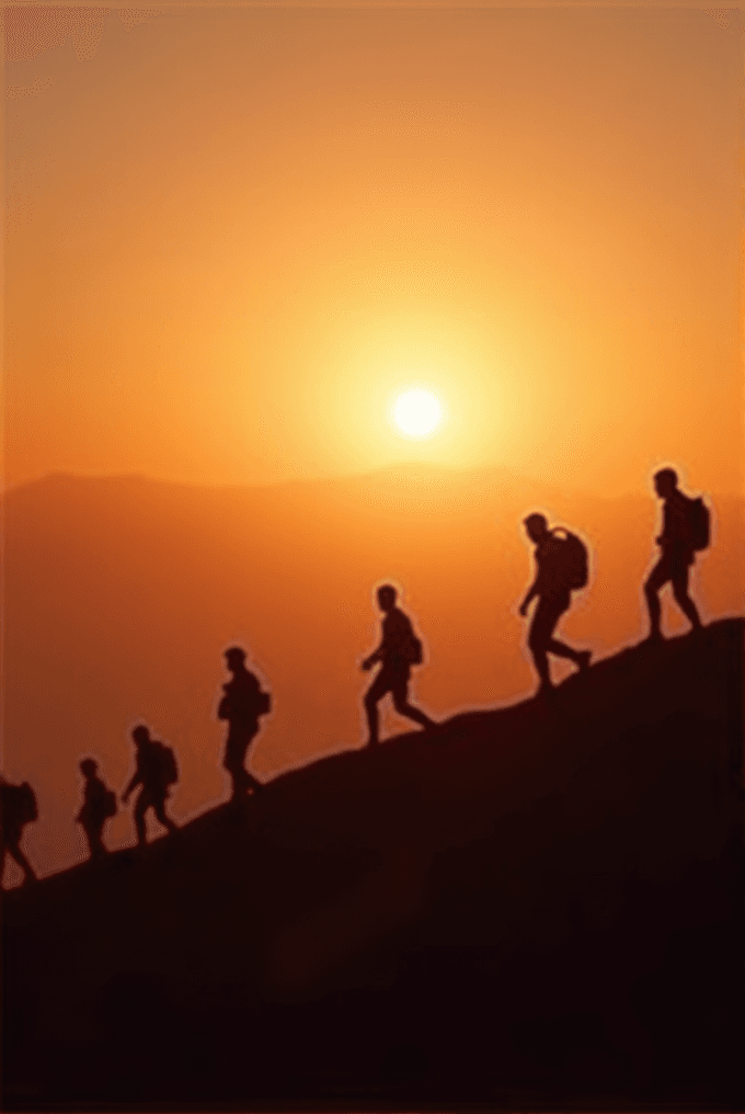 Silhouetted hikers walk up a hill against a vibrant orange sunset.