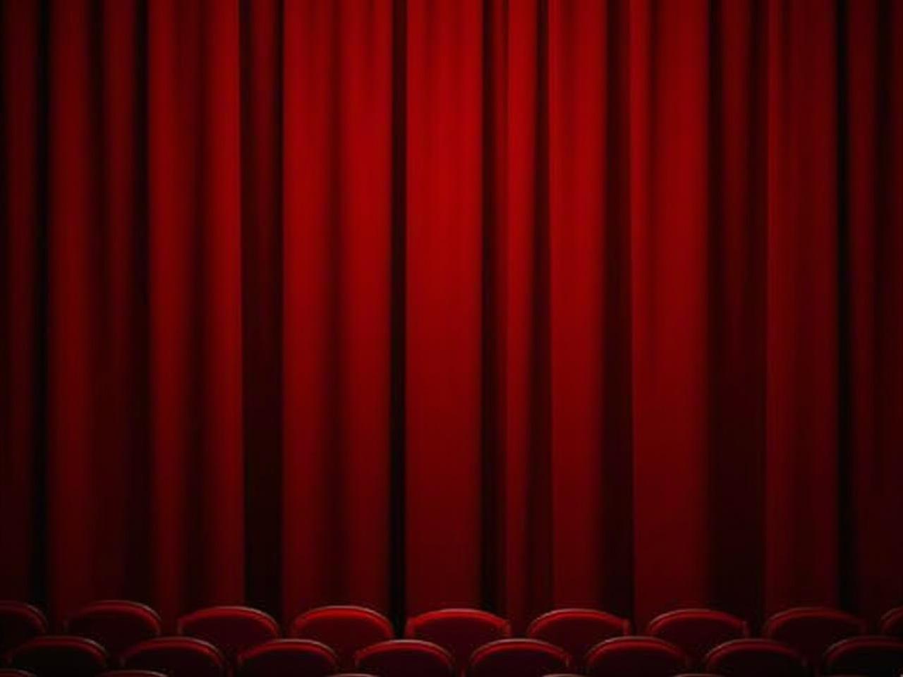 The image shows a red velvet curtain in a theater setting, gracefully draping down in vertical folds. The curtain is rich in color, creating a warm and inviting atmosphere. In front of the curtain, there are rows of empty red seats, indicating that the theater is ready for an upcoming performance. The lighting casts a soft glow on the curtain, enhancing its texture and depth. This scene evokes anticipation and excitement for the show to begin.