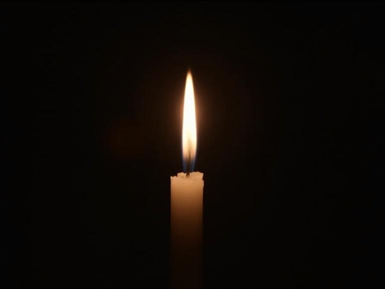 Close-up of a flickering candle in total darkness. Soft warm light dancing with a slight camera shake. Suspenseful mood.