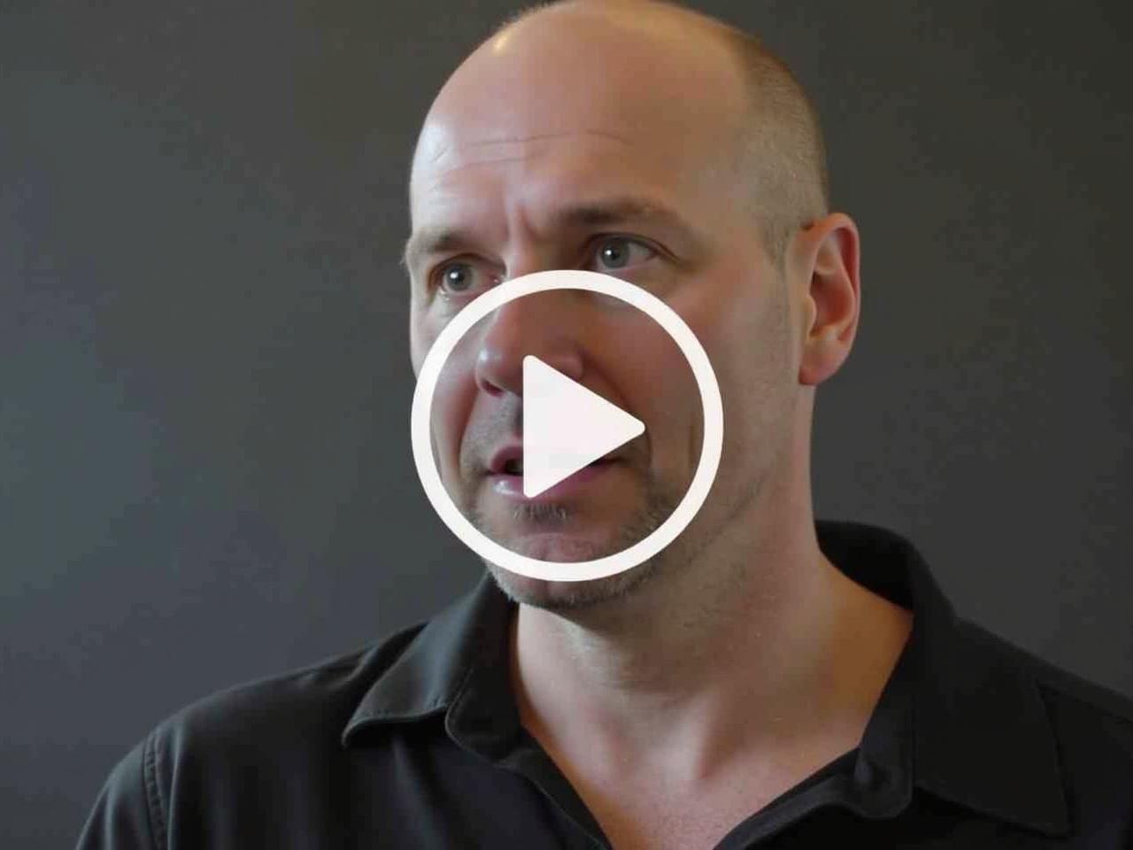 This video cover depicts a man with a confident expression, discussing the first law of power. The background is dark, emphasizing the speaker's face. He is dressed in a casual black shirt, and his direct gaze conveys authority. A play button overlay indicates that this is a video. The focus is on engaging the audience with insights about power dynamics. This visual is aimed at attracting viewers interested in self-improvement and leadership strategies.