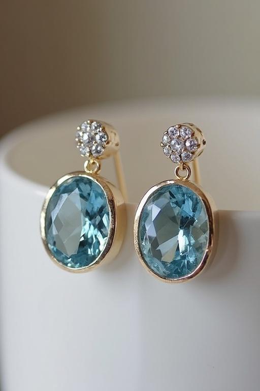 Aquamarine earrings in a close-up view. Earrings have a gold finish with a large aquamarine stone and smaller sparkling stones on top. Soft background enhances focus on earrings.