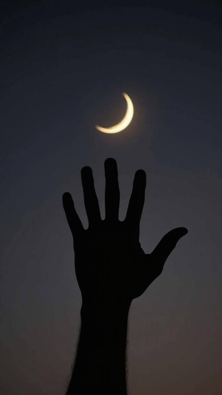 A silhouette of a hand reaching towards a crescent moon at dusk.