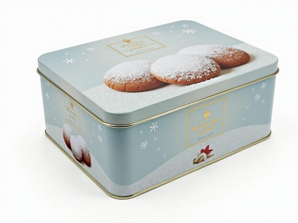 The image shows a rectangular tin box with a winter-themed design. The lid of the box features subtle snowflakes and images of cookies dusted with powdered sugar. The box appears to be made of metal and has a light, frosty color scheme, giving it a festive look. On the side of the box, there is a label that reads "Wiener Zucker," a brand associated with sugar products. This type of tin is often used for storing holiday cookies or confectioneries.