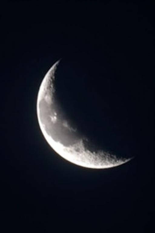 Crescent moon glowing against dark night sky. Detailed craters and surface textures visible.