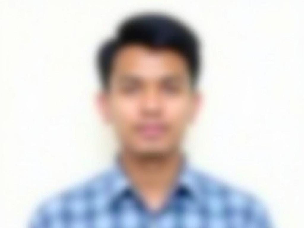 The image shows a person with a blurred face, wearing a blue and white checked shirt. He has short black hair that is styled upward. The background is plain white, which creates a clean and neutral look. The individual is posing directly at the camera in a frontal view. This image seems to be a professional portrait, likely taken for a resume or identification purpose.