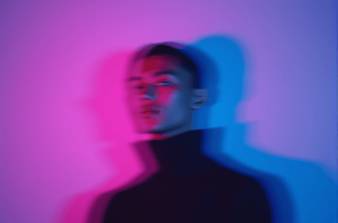 A person in a black turtleneck is blurred with vibrant pink and blue lighting creating a dreamy effect.